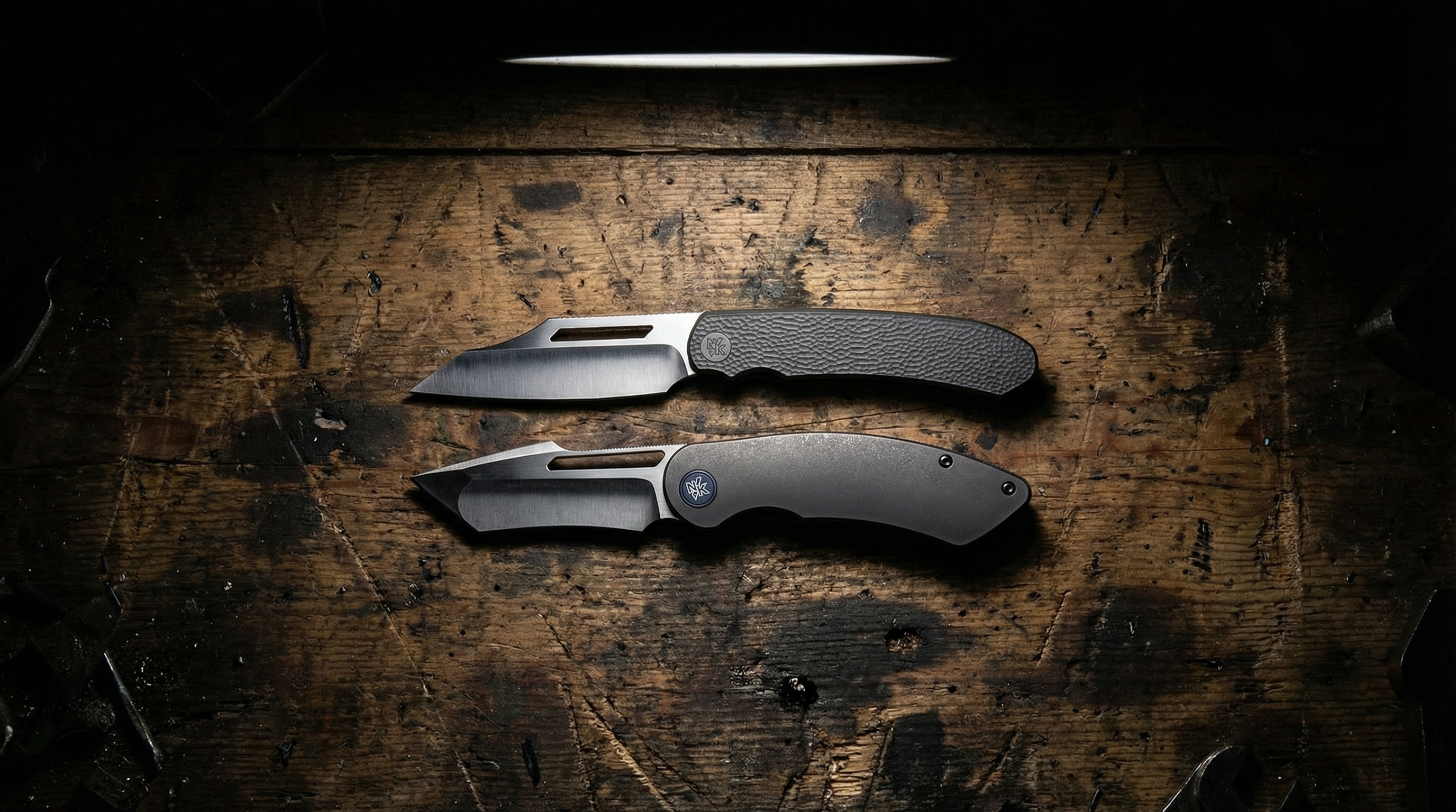 Two Neeve Knife Co. folding knives on a worn wooden surface with a dark background