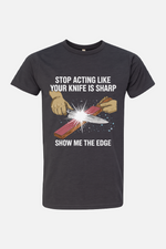 Gray t-shirt featuring a graphic of hands sharpening a knife on a stone with spark effects, with the text “Stop Acting Like Your Knife Is Sharp” above and “Show Me the Edge” below.